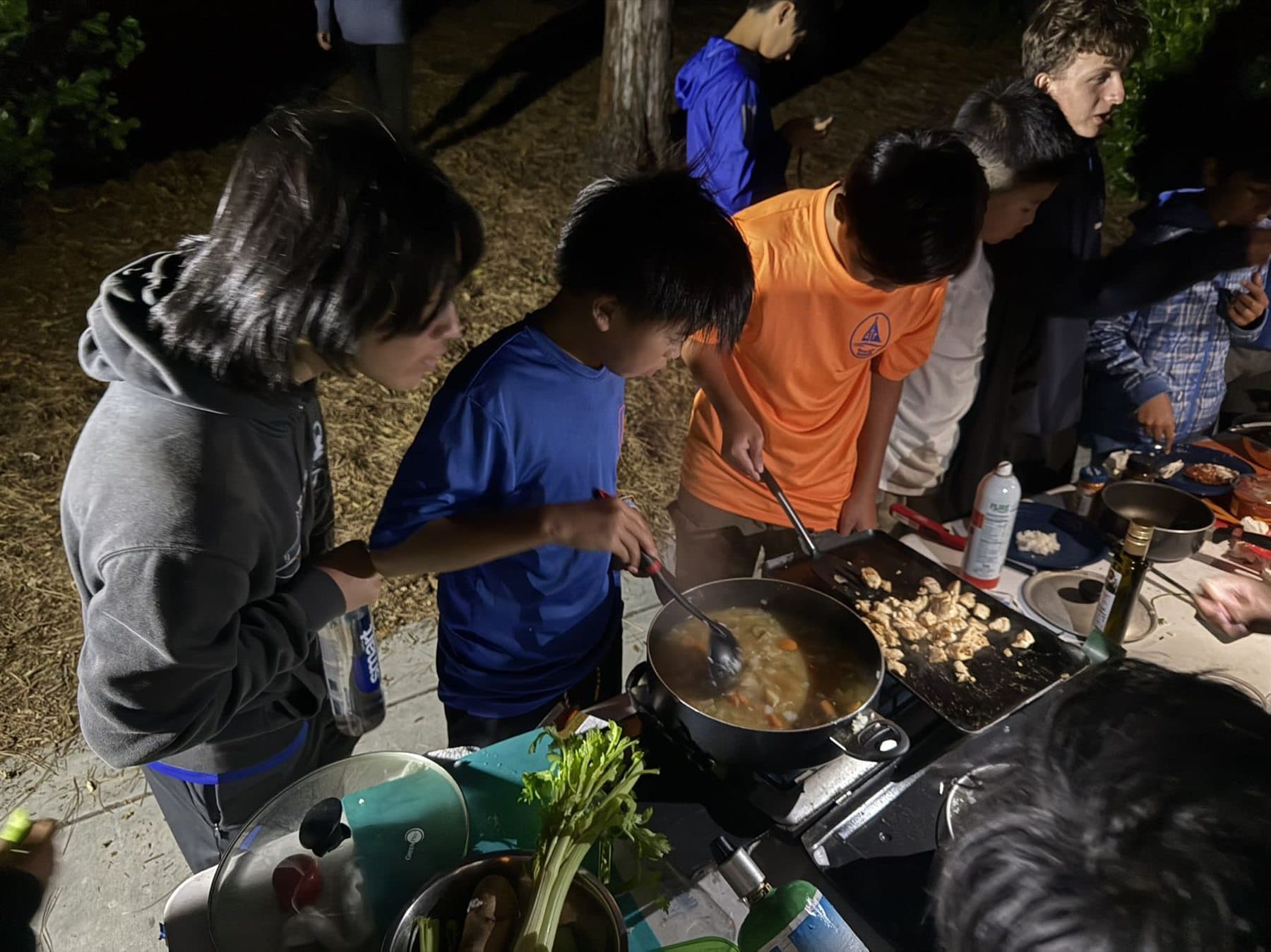 Scouts cooking together outdoors at night during a campout